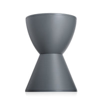 The Kartell Prince Aha Stool, featuring a modern hourglass shape in gray with a smooth top and ribbed lower half, can also be used as a versatile side table and is shown elegantly displayed on a white background.