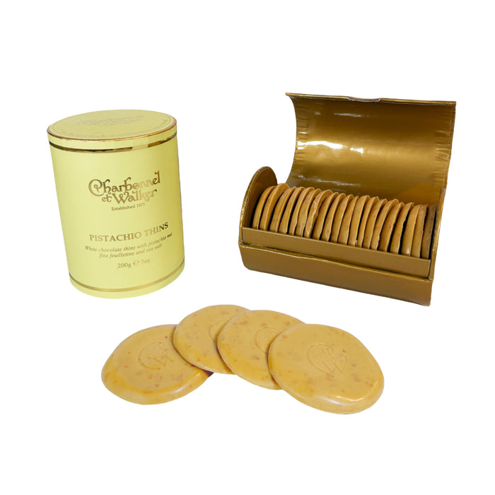 A cylindrical box and an open rectangular container filled with Charbonnel & Walker Pistachio Thins, 200g, with four individual chocolates arranged in front.