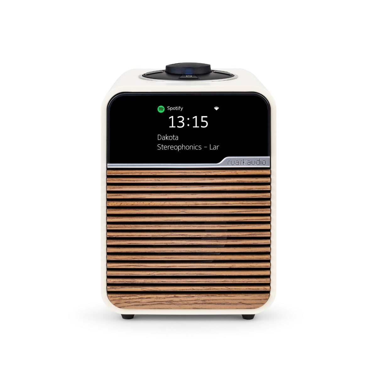 The Ruark R1S Smart Radio by Ruark is a compact, modern tabletop speaker with a wood slat front and white casing. Its digital display shows the time (13:15), now playing "Dakota" by Stereophonics, and Wi-Fi radio for seamless streaming.