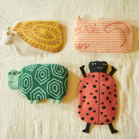 Four small, soft toys shaped like a snail, a cat, a turtle, and a ladybug are arranged on a cream-colored fabric background, conjuring the cozy charm of Donna Wilson’s Ladybird Hot Water Bottle.