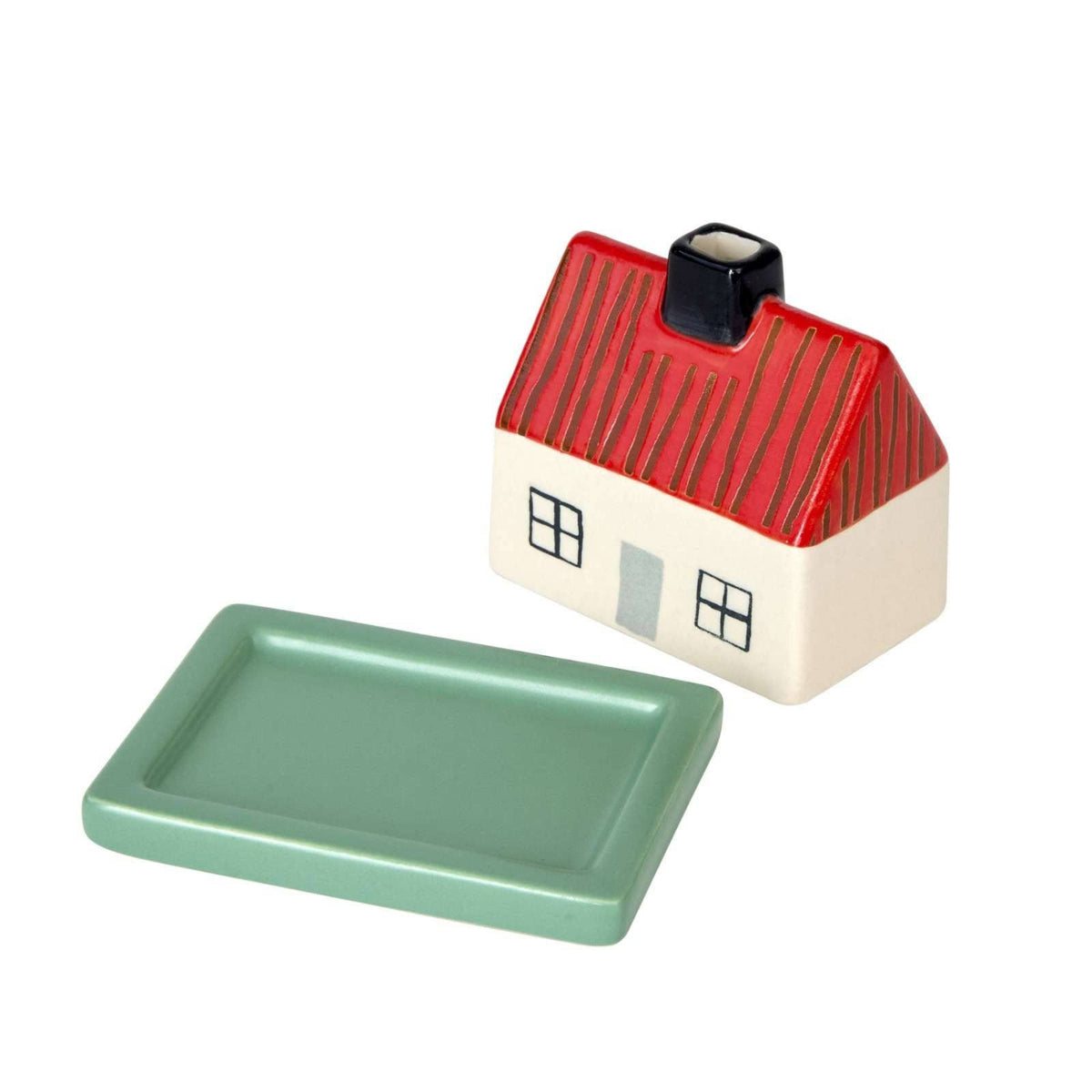 Donna Wilson’s Little Hiding House by Donna Wilson is a charming stoneware butter dish shaped like a small house with a red roof and a green rectangular base, set against a white background.