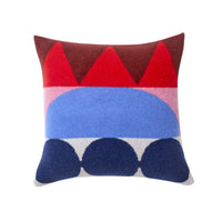 The Totem Large Square Cushion – Red by Donna Wilson is a decorative square pillow made in the UK. It features a bold, colorful abstract pattern with geometric shapes such as triangles, half-circles, and bands in red, pink, blue, navy, and white. Crafted from soft lambswool, this cushion brings vibrant style to any space.