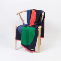 A Sophie Home Bruten geometric throw in bold navy, red, green, and blue draped over a wooden armchair.