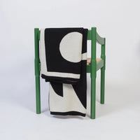 Black and white Sophie Home Bruten Throw with a bold geometric circle pattern draped over a green wooden chair.