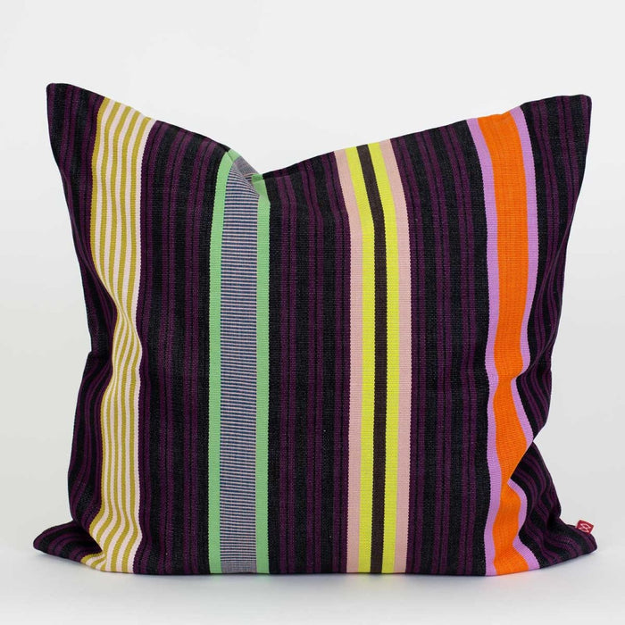 The Hana Cushion by World Of Craft is a square, handwoven piece crafted by a Guatemalan artisan, featuring black and purple stripes with colorful vertical accents in yellow, green, white, orange, and lavender on one side. It is photographed against a plain white background.