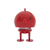 A red Hoptimist Bumble Desk Toy with a spring neck, two eyes, and a small nose standing on two feet, styled as classic Danish design desk decor.