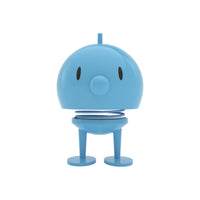 Light blue Hoptimist Bumble Desk Toy on a spring, featuring a large head, small nose, and two feet as a piece of Danish design.