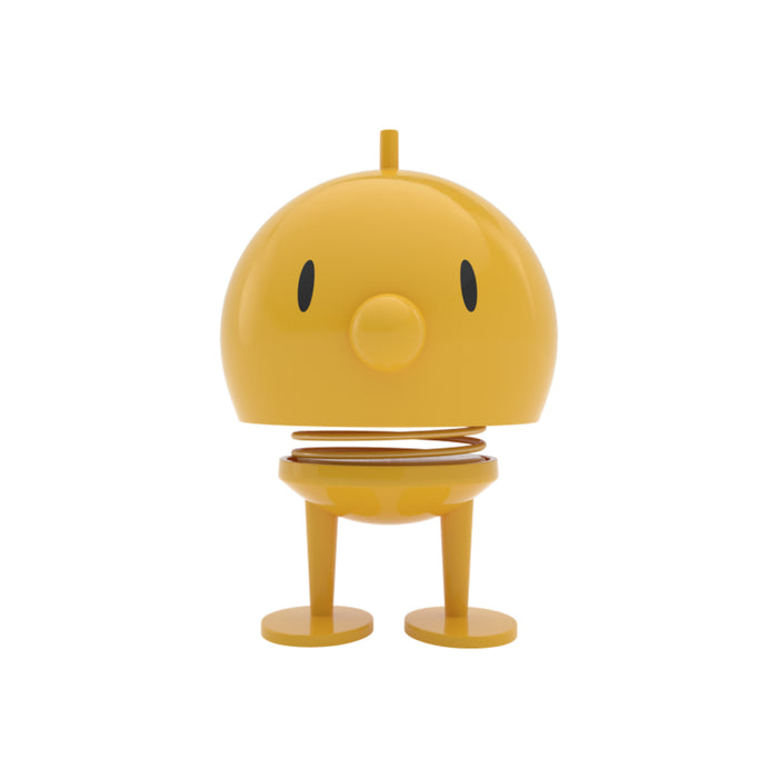 Yellow round Hoptimist Bumble desk toy with a spring-mounted head, two simple eyes, a round nose, and two feet.