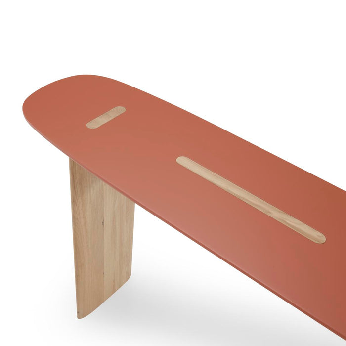 A long, terracotta-colored Ligne Roset Intervalle Console Table with a rounded top, light wood legs, and two inlaid wooden slots on the surface.