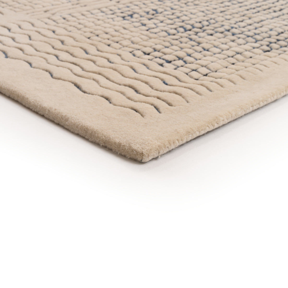 A corner of a beige Ligne Roset Katagami rug featuring a raised, bouclé grid pattern of blue squares and wavy lines.