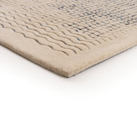 A corner of a beige Ligne Roset Katagami rug featuring a raised, bouclé grid pattern of blue squares and wavy lines.