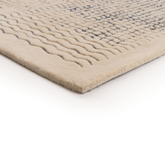 A corner of a beige Ligne Roset Katagami rug featuring a raised, bouclé grid pattern of blue squares and wavy lines.