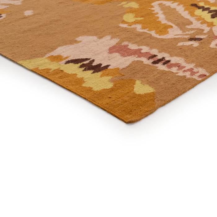 A corner of a hand-tufted Ligne Roset Kimono rug featuring an abstract, multicolored pattern in earthy tones of mustard, brown, and cream.