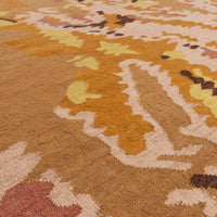 An angled, close-up view of a flat-weave Ligne Roset Kimono rug featuring an abstract pattern in shades of gold, brown, and cream.