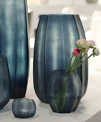 A set of Guaxs Koonam Vases in Ocean Blue/Indigo, crafted from mouthblown glass in matte translucent shades and varying heights, is displayed. One vase holds pink and white ranunculus flowers with green stems.