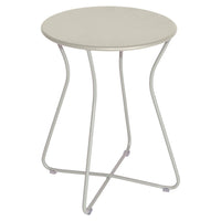 The Fermob Cocotte Side Table is a small, round outdoor table in light gray, made of weatherproof steel with a smooth top and four slender, curved legs that cross at the base for stability.