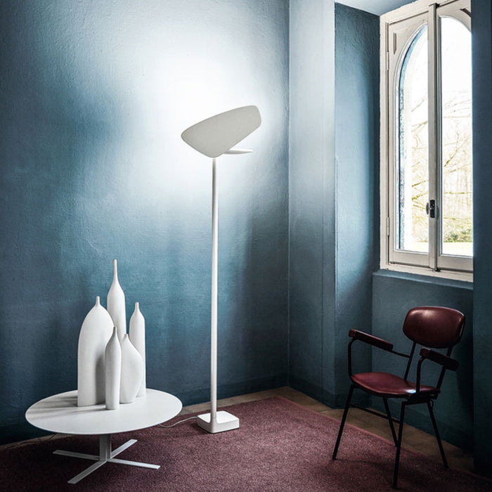 Ex-Display Lightwing Floor Light in white with a wide, angled shade glowing in a room corner next to a round table with four white vases and a red armchair.