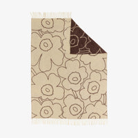 The Piirto Unikko Blanket by Marimekko is a beige wool throw adorned with large brown-outlined floral patterns and fringe on two ends. A corner is folded over to display its brown underside, featuring beige flower outlines. Crafted to meet the Responsible Wool Standard, this blanket combines ethical craftsmanship with the timeless appeal of Marimekko’s iconic design.