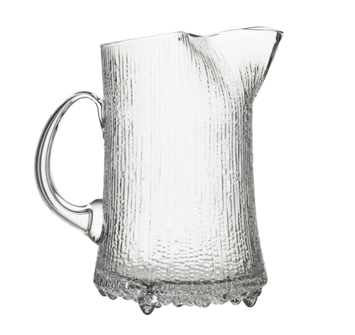 The Ultima Thule Pitcher 150cl features mouth-blown glass with a textured surface, curved handle, and wavy spout. Its base is decorated with small raised glass beads, reflecting Iittala’s signature style.