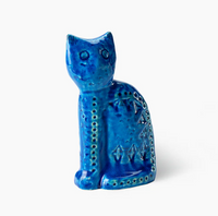 The Seated Cat Figure by Bitossi is a blue ceramic figurine with a glossy finish, mid-century design, and indented geometric patterns, inspired by Rimini Blu. The cat sits upright against a plain white background.