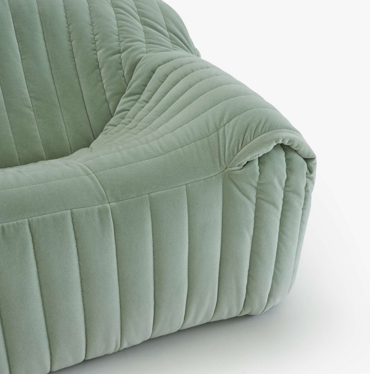 Close-up of the Sandra Small Sofa by Ligne Roset in light green velvet, featuring deep vertical quilting and plush cushioning for a retro-inspired look, shown on a white background.