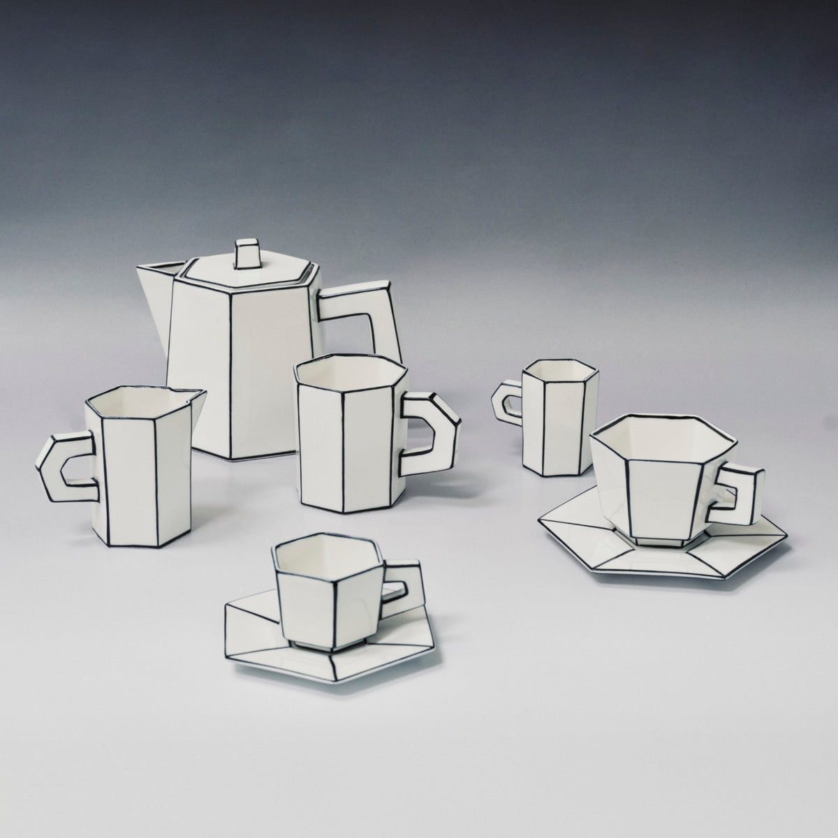 Six white, angular pieces—including cups, saucers, a teapot, and a creamer—crafted from fine bone china and featuring bold black outlines reminiscent of 2D cartoon drawings, are displayed on a plain surface with a gradient background. These pieces are part of the Carte Blanche Cup and Saucer Set of 2 by Serax.