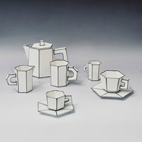 Six white, angular pieces—including cups, saucers, a teapot, and a creamer—crafted from fine bone china and featuring bold black outlines reminiscent of 2D cartoon drawings, are displayed on a plain surface with a gradient background. These pieces are part of the Carte Blanche Cup and Saucer Set of 2 by Serax.