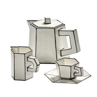 Three white ceramics—a Carte Blanche Teapot by Serax, a creamer, and a cup with matching saucer—stand out with bold black outlines and exude modern artistry in fine bone china. Each Serax piece showcases angular, geometric forms and a strikingly contemporary design.