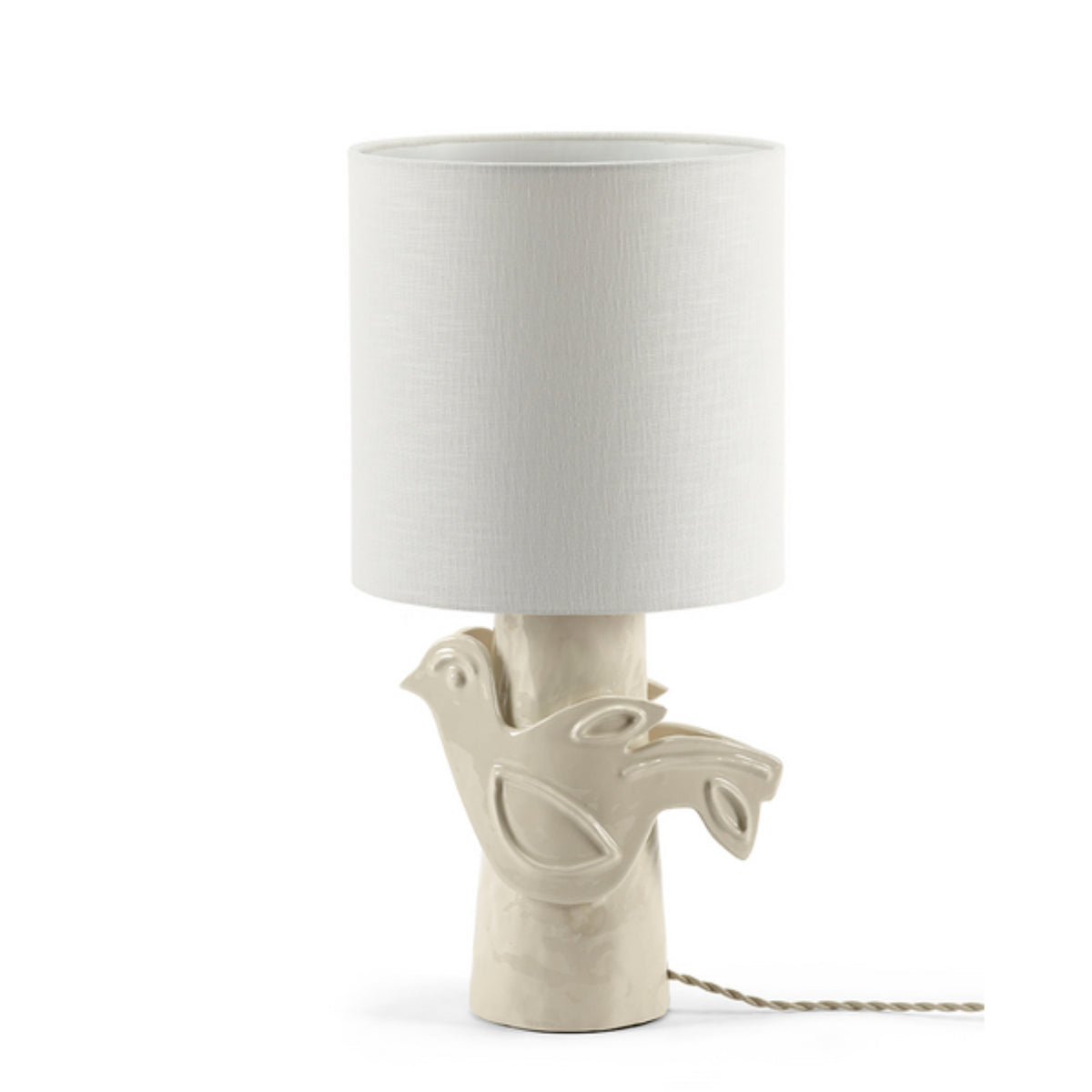 The Paloma Table Lamp in white by Serax is a handcrafted piece featuring a ceramic base shaped like a dove perched on a branch and topped with a cylindrical fabric shade; the power cord remains visible.