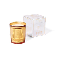 A Trudon Holiday Candle 270g in a gold-tinted glass jar with an embossed emblem, displayed beside its white and gold Christmas box.