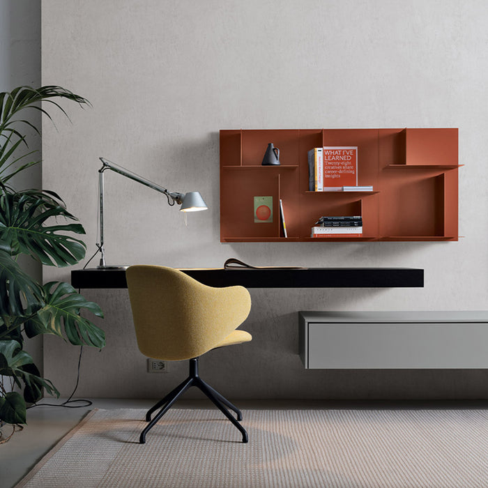 A modern minimalist workspace with a floating black desk, yellow swivel chair, silver desk lamp, potted plant on the left, and Kristalia’s Avenue Library Shelving and an orange wall shelf displaying books and decor against a light wall.