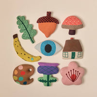 Donna Wilson’s Acorn Shaped Cushion is one of nine vibrant, soft fabric plush shapes—including an oak leaf, mushroom, banana, eye, house, artist palette, thistle flower, and cherry blossom—expertly knitted in Scotland from the finest materials and presented in a 3x3 grid against a neutral background.