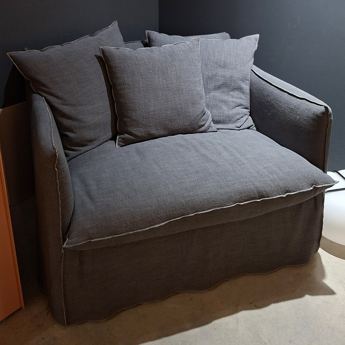 A gray Gervasoni Ex-Display Ghost Single Sofa Bed 11 with three matching cushions and a removable cover sits against a dark wall on a light concrete floor.