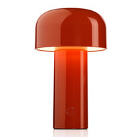 The Flos Bellhop Portable Lamp, IP54, features a modern glossy red finish, cylindrical base, large rounded dome shade, emits warm cordless light, is rechargeable, and includes a small circular button on the base.