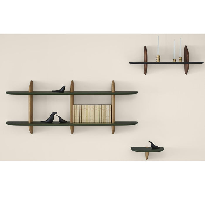 Three minimalist, mid-century modern Intervalle Shelves, Large by Ligne Roset are mounted on a beige wall. Two shelves hold black bird figurines, one shelf displays books, and the top shelf showcases three candlesticks with white candles. The Intervalle Shelving features dark surfaces and wooden vertical supports, creating elegant wall-mounted shelves that seamlessly blend style and function.
