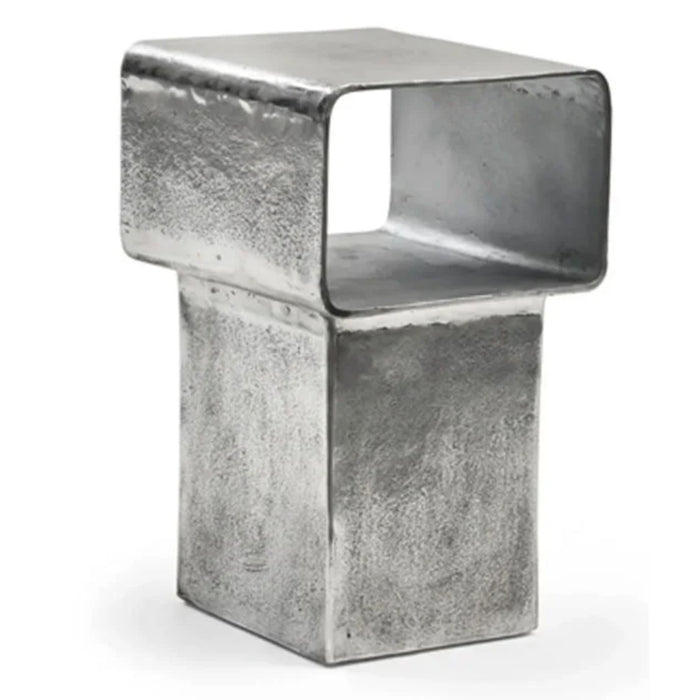 The Kira Side Table by Gervasoni features a modern, metallic silver finish in cast aluminum, with a rectangular hollow top and solid base, plus a textured industrial look inspired by contemporary sculpture.