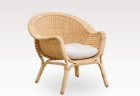 The Madame Lounge Chair by Sika Design is a light brown rattan lounge chair with curved armrests and legs, featuring a rounded back and a white cushioned seat, set against a plain light background.