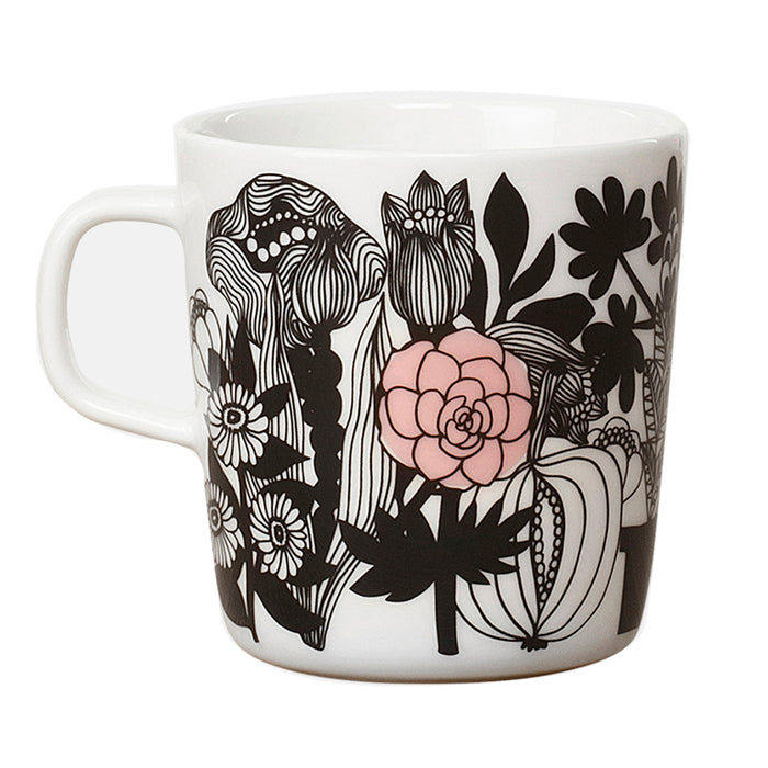 The Marimekko Oiva Siirtolapuutarha Mug is a white ceramic mug featuring the distinctive Siirtolapuutarha pattern with stylized black flowers and leaves, accented by a single pink flower on the side. This bold and artistic botanical design creates vibrant visual interest, making it a standout piece reminiscent of Marimekko’s iconic style.