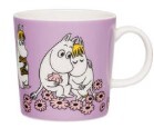 The Arabia Moomin Mug - Sweethearts is a purple ceramic mug featuring Tove Jansson's beloved Moomin characters sitting among pink flowers, with one character hugging another.