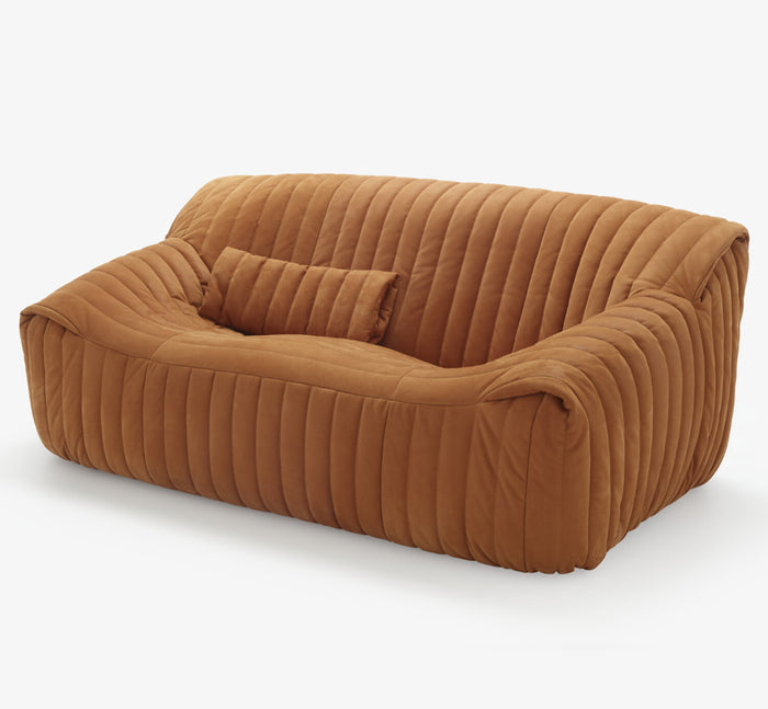 The Sandra Small Sofa, Vidar by Ligne Roset features modern brown velvet upholstery, vertical quilting, rounded edges, and a matching pillow, shown on a plain white background.