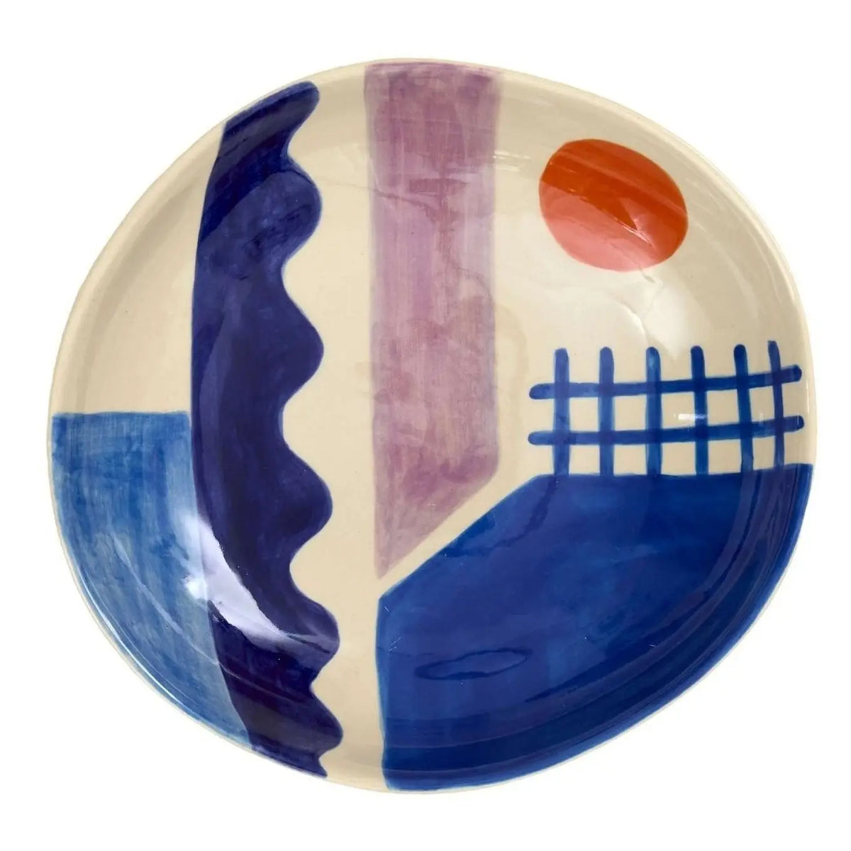 A hand-painted stoneware serving bowl from Donna Wilson, the Sun + Sea Serving Bowl features abstract designs with blue shapes, a wavy stripe, a purple vertical stripe, a grid pattern, and an orange circle on a cream background—capturing the playful aesthetic characteristic of Donna Wilson’s collections.