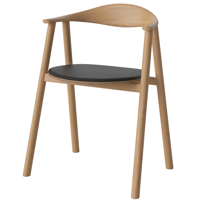 The Bolia Swing Dining Chair, Upholstered, features Scandinavian design with a solid oak frame, angled legs, curved backrest, and round black seat cushion for a minimalist look with light wood and an open silhouette.
