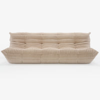 A modern, plush beige Togo Very Large Sofa by Ligne Roset, crafted in Phlox fabric and inspired by Michel Ducaroy’s iconic design, featuring deep horizontal and vertical tufting, a low-profile silhouette, and overstuffed cushions—shown here on a white background.